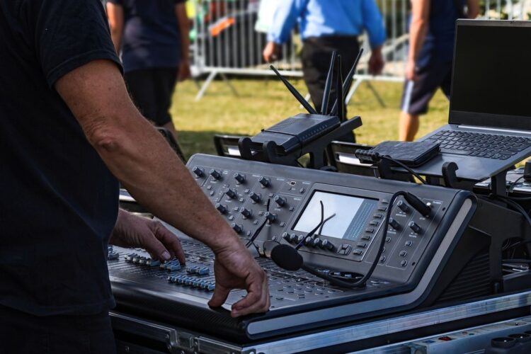 Sound engineer operating an outdoor mixing console beside a laptop
