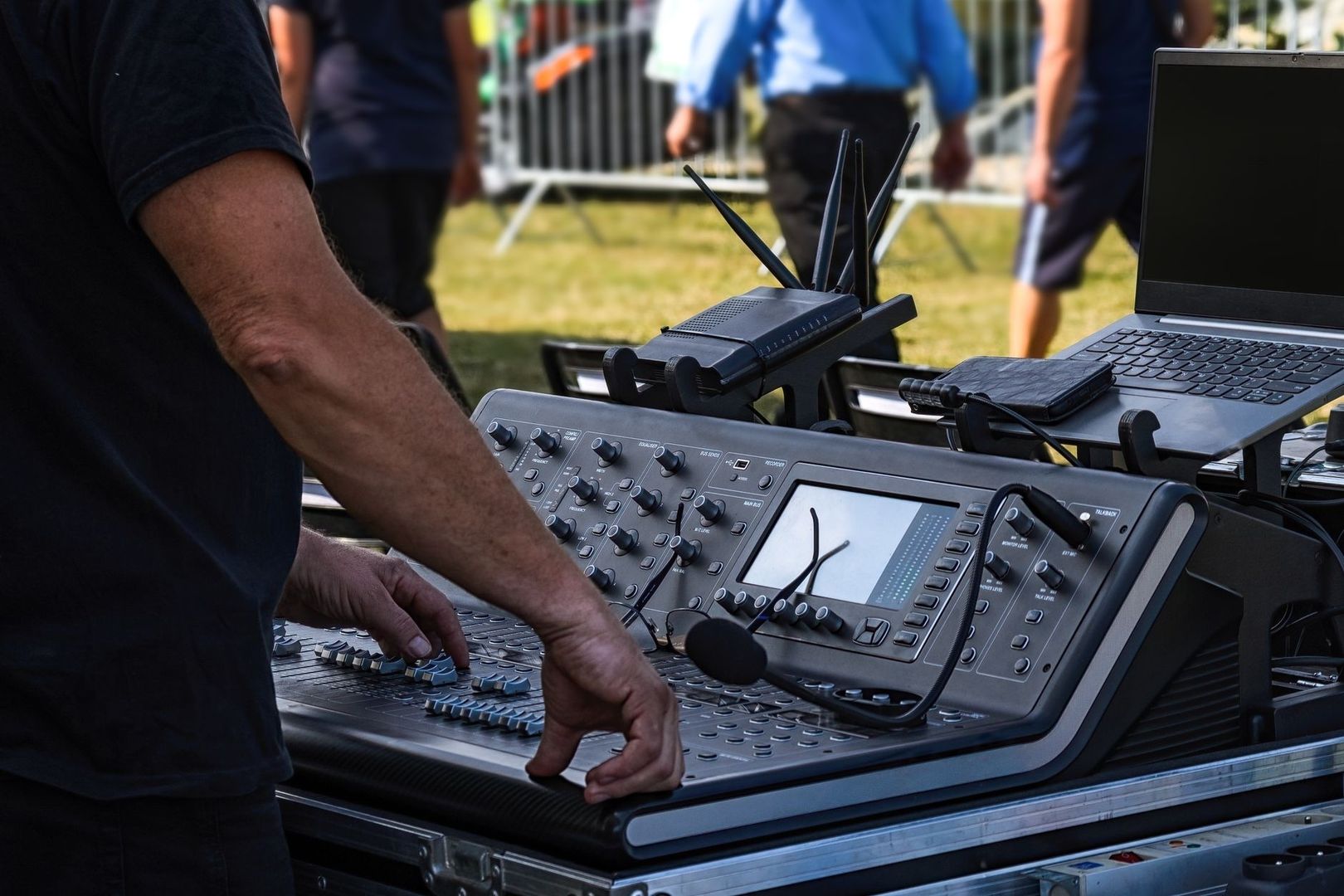 Sound engineer operating an outdoor mixing console beside a laptop