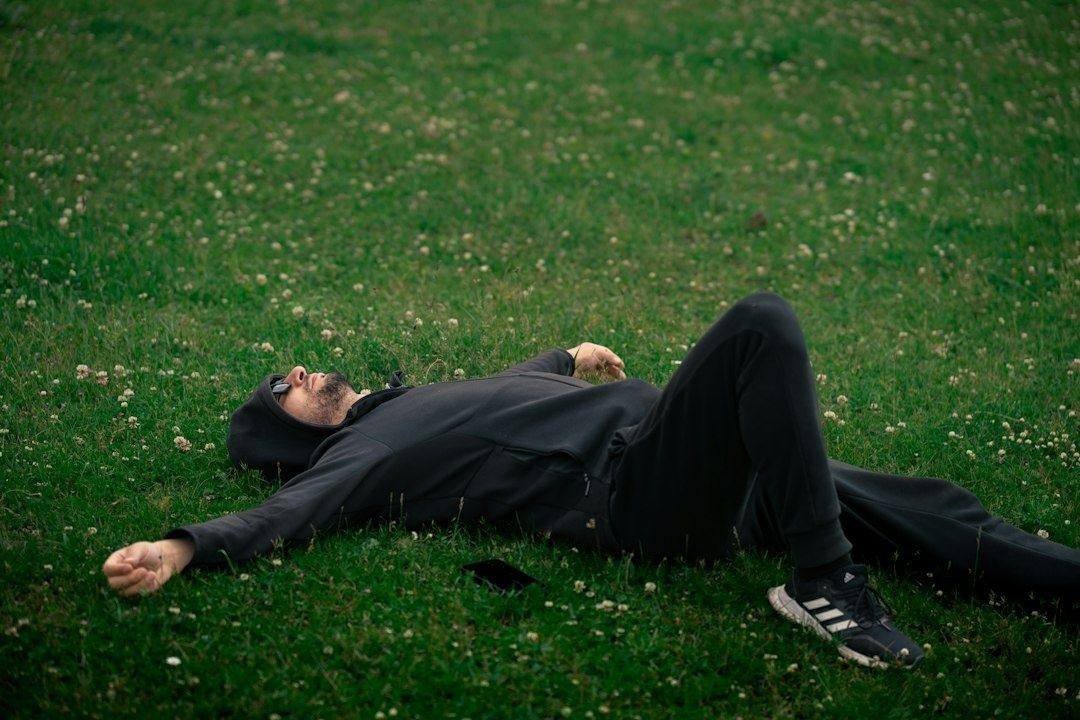 Tired person in black clothing lying on a clover-covered lawn